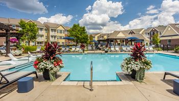 A pool surrounded by flowers and chairs with apartment buildings in the background.